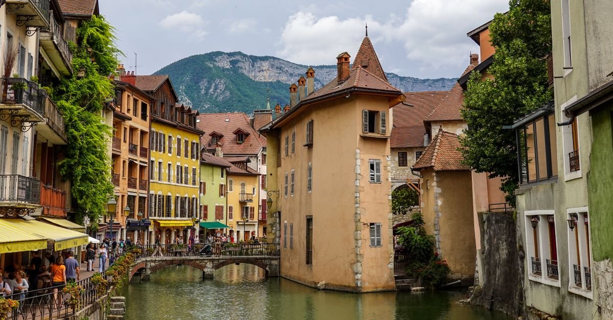 Canal bordé de bâtiments anciens dans une ville historique des Alpes, avec les montagnes en arrière-plan