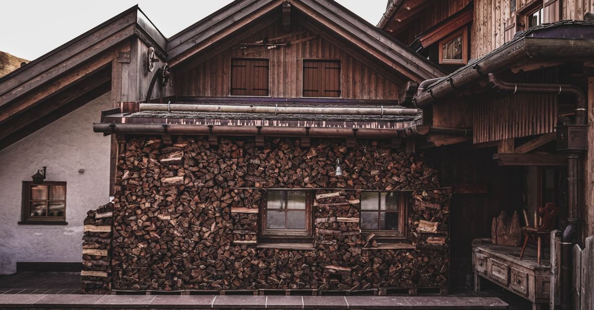 Façade d'un chalet en bois avec bardage ancien et pile de bûches contre le mur