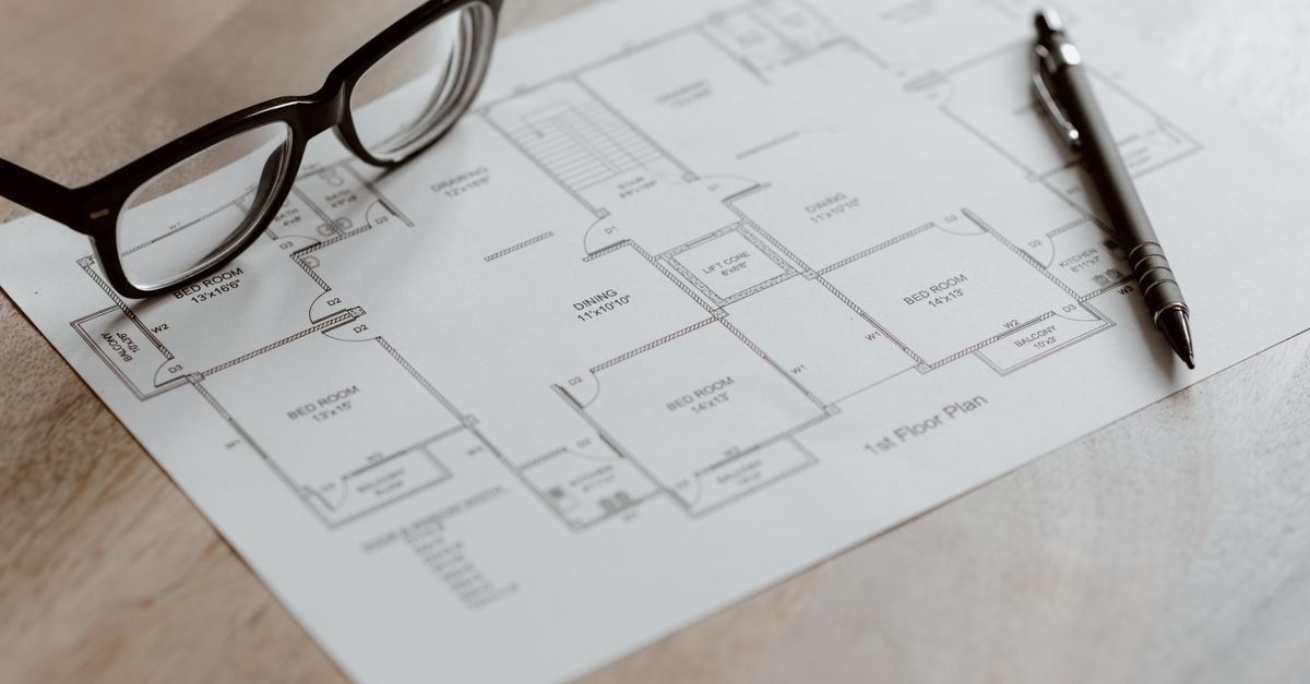Plan d'aménagement d'une pièce posé sur une table en bois avec un stylo et une paire de lunettes